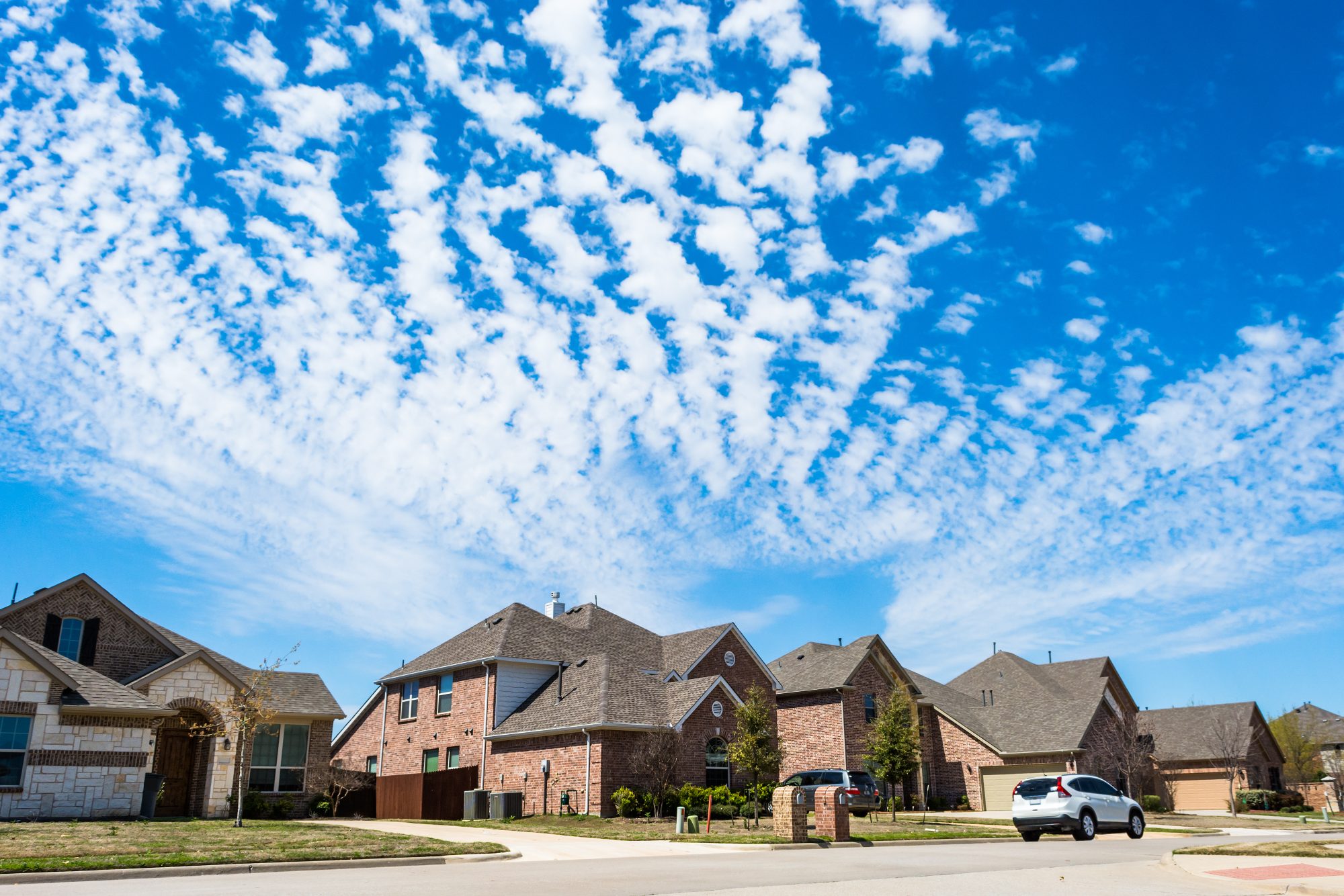 Suburban residential street with brick homes under blue sky and white clouds