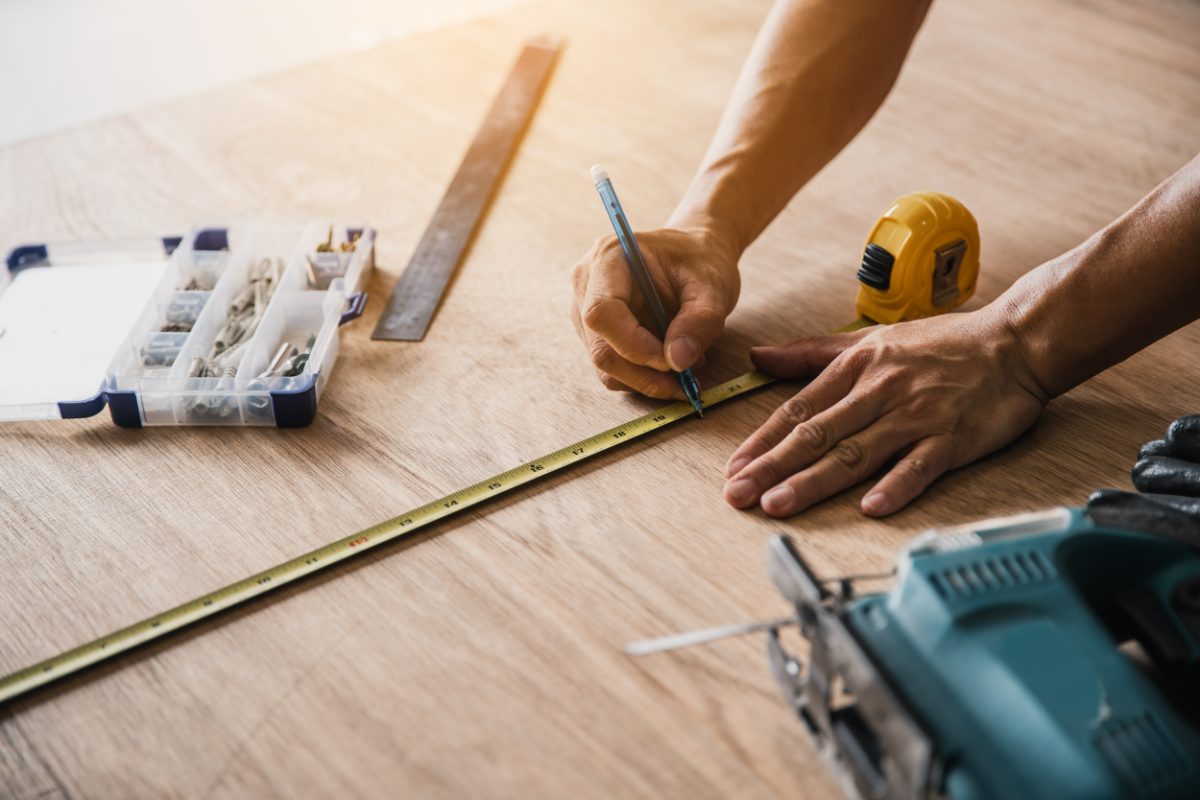 Carpenter measuring wooden flooring with tape measure and pencil, tools nearby