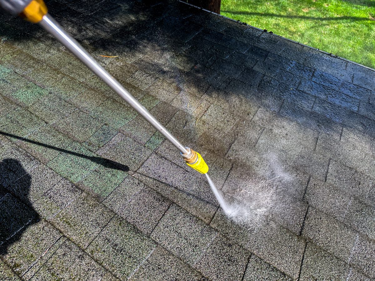 Pressure washer cleaning moss and dirt from asphalt roof shingles with yellow nozzle
